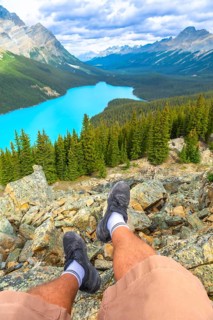 Hiker resting on a rocky mountain top, soaking in the stunning panoramic view of turquoise peyto