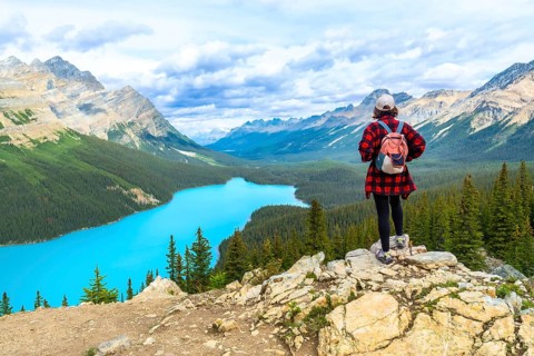 Female hiker standing on a rocky cliff, gazing at the turquoise waters of peyto lake and the