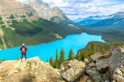 Hiker standing on a rocky cliff, overlooking the turquoise waters of peyto lake, surrounded by