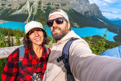 Two happy tourists are taking a selfie with peyto lake and the canadian rockies in the background