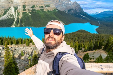 Tourist with a backpack and sunglasses taking a selfie at the scenic viewpoint of peyto lake in