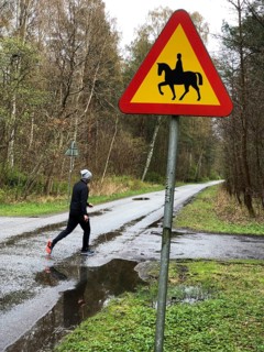 Person jogging on wet forest road with road sign for riding on horse in Ystad, Skåne County,