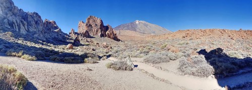 Barren rocky landscape with blue sky, dry vegetation and impressive Pico del Teide in the