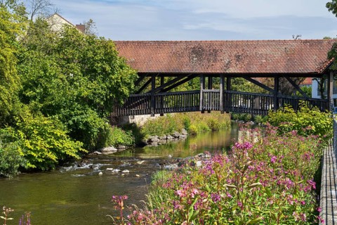 Covered footbridge over the Kronach river, hospital bridge, Blooming flowers on the shore, Kronach,