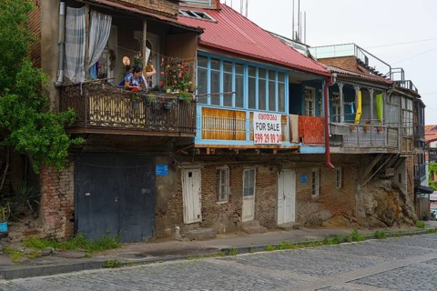 Dilapidated residential buildings with sales signs and rustic balconies on a paved street, Old