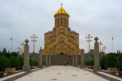 Grand cathedral with golden roof and stylish stone pillars against cloudy sky, Sameba Cathedral,