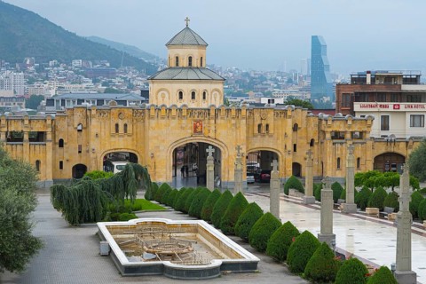 Historic church with yellow tone and modern city in the background against mountain backdrop,