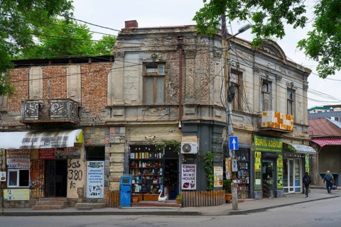 An old building corner with shops on the street, surrounded by trees and power lines, Tbilisi,