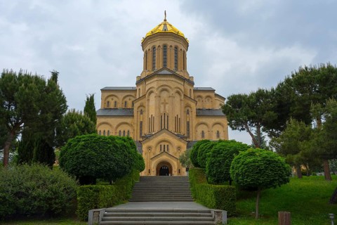 A magnificent church with a golden dome and symmetrical steps surrounded by lush greenery, Sameba
