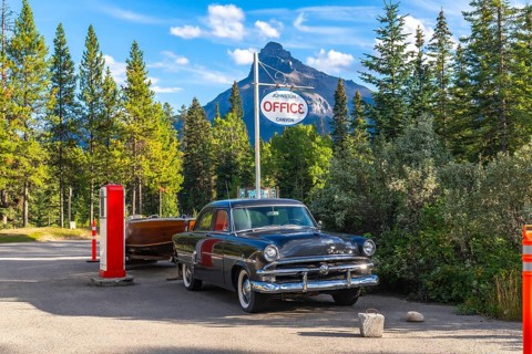 Vintage car towing a wooden boat trailer parked near a vintage gas pump by the johnston canyon