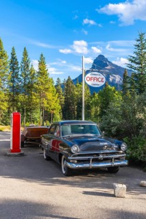 Classic car with a wooden boat parked in front of the johnston canyon office sign, with castle