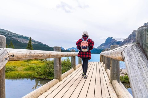 Female tourist walking on a wooden bridge enjoying the breathtaking view of bow lake and