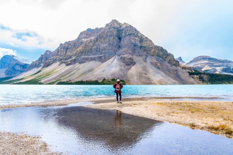 Female hiker stands at the edge of bow lake, admiring the turquoise water and imposing mountain