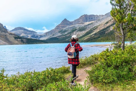 Female tourist with backpack walking along hiking trail by turquoise bow lake with crowfoot glacier