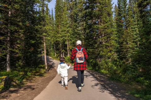 Mother and child holding hands, enjoying a leisurely hike along a paved path, surrounded by the