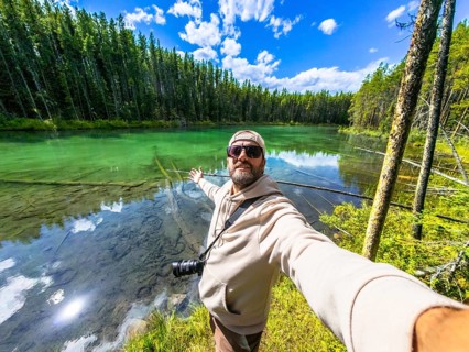 Photographer taking a selfie with outstretched arms at herbert lake, surrounded by turquoise water,