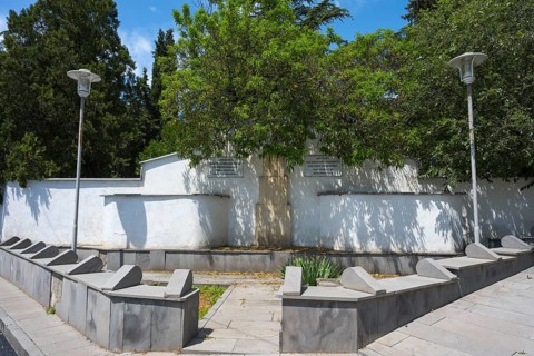 Small park with memorial and trees, surrounded by a white wall, modern lanterns illuminate the