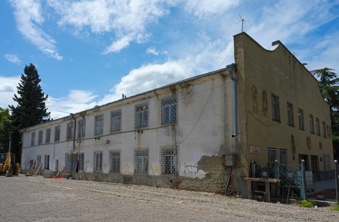 Old, dilapidated building with lattice windows under cloudy sky, excavator in the foreground,