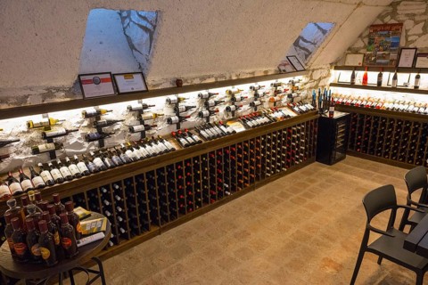 Wine cellar with illuminated shelves full of wine bottles and simple chairs and tables for