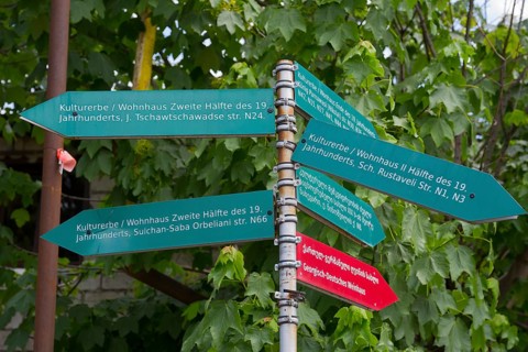 Green signpost with signs showing the cultural heritage of the 19th century under trees, Bolnissi,