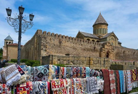 Rugs in front of a historic wall with a cathedral in the background under a blue sky,