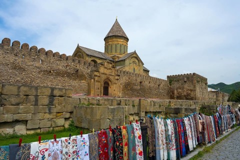 Stone fortress with monastery in the background, lots of colorful fabrics hung in front of it,