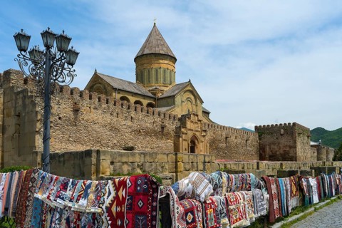 Rugs in front of a historic wall and a church under a blue sky, Svetitskhoveli Cathedral,
