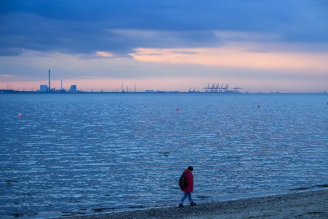 Person on the beach with a view of the sea and industrial areas in Wilhelmshafen right Jade-Weser