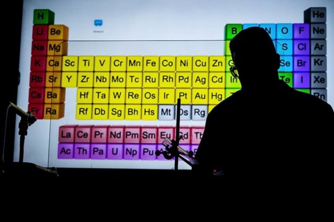 Silhouette of a chemistry teacher in front of an illuminated projection of the periodic table in