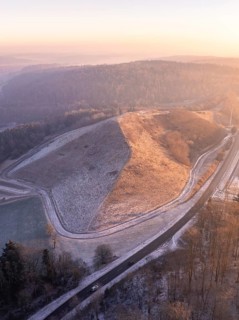 Aerial view of a hill in morning light with snow-covered roads and surrounding forest, future PV