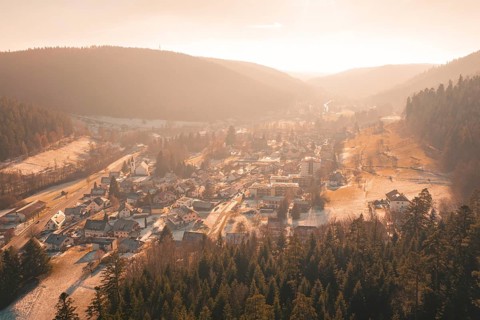 Panoramic view of a village with snow-covered roofs surrounded by forests and hills in the evening