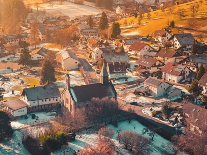 Village in winter with a central church surrounded by houses, hills and soft, warm light,