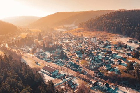 Extensive aerial view of a valley with snowy houses surrounded by mountains and warm sunset light,