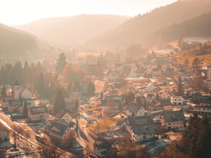 A picturesque village is situated in a valley surrounded by hilly forests and gentle autumn fog,
