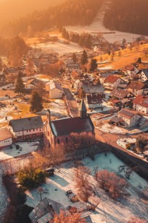 Snowy village with central church, warm sunlight bathes the surrounding area in golden tones,