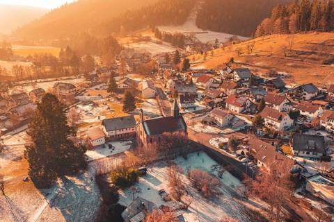 Snowy village with central church surrounded by snow-covered houses and warm golden light,