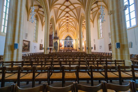 Extensive church space with Gothic vaults, wooden chairs and an altar in the center, collegiate