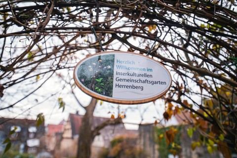 Wooden sign with welcome text for the intercultural community garden surrounded by branches,