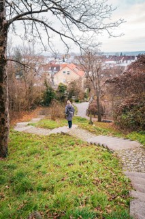 A woman walks down a stone staircase surrounded by trees and autumn leaves in an urban park,