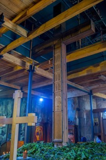 Interior with wooden cross, wooden beams and plants under artificial light, Javari Monastery,
