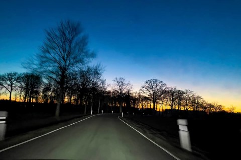 View from speeding speeding car at dusk at nightfall on a country road illuminated by headlights