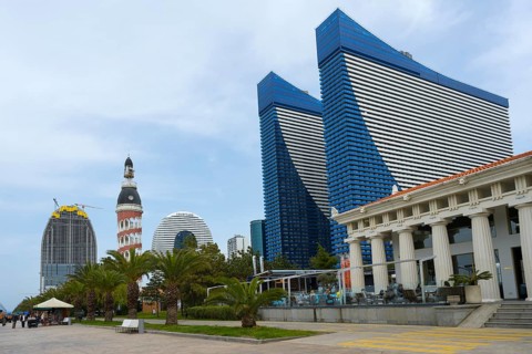 Skyscrapers with blue glass facades next to palm trees and column-supported buildings shape the