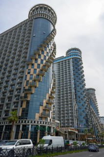 Modern skyscrapers with spiral balconies dominate the city skyline under cloudy sky, Orbi Sea