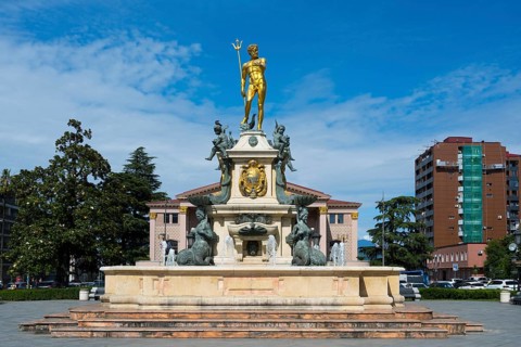 A fountain with a golden Neptune statue surrounded by water figures in front of a building, Neptune