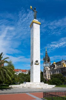 Tall column with statue in a square next to a magnificent building and tower, statue of Medea,