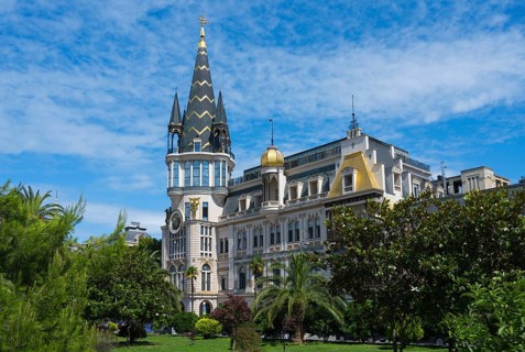 Castle-like building with tall tower and green garden under blue sky, Astronomical Clock, Black