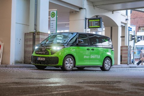 Green VW shuttle at a bus stop, modern urban atmosphere, Deer E-Mobility Shuttle Service, Calw,