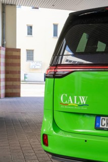 Green car in city scene with 'Calw' lettering on the back, Deer E-Mobility Shuttle Service, Calw,