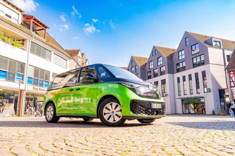 Green car in an urban square with blue sky in the background, Deer E-Mobility Shuttle Service,