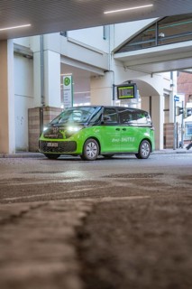 Green shuttle goes around a bend in an urban area, busy atmosphere, Deer E-Mobility Shuttle